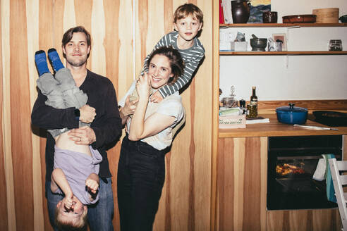 Porträt von lächelnden Eltern, die mit ihren Söhnen spielen, während sie in der Küche zu Hause stehen - MASF42559