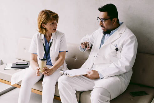Oberarzt im Gespräch mit einem jungen männlichen Kollegen auf dem Sofa im Krankenhaus - MASF42598