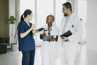 Smiling multiracial healthcare workers discussing while standing at hospital - MASF42610