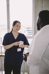 Smiling female nurse holding coffee cup while looking at doctor in hospital - MASF42621