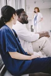 Seitenansicht von männlichen und weiblichen medizinischen Kollegen, die in der Krankenhauscafeteria sitzen - MASF42622