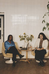 Portrait of smiling businesswomen sitting together on chairs at office - MASF42642