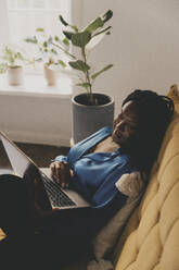 Businesswoman working on laptop while reclining on sofa at home - MASF42663