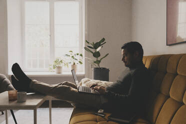 Geschäftsmann, der einen Laptop benutzt und auf dem Sofa im Büro sitzt - MASF42665