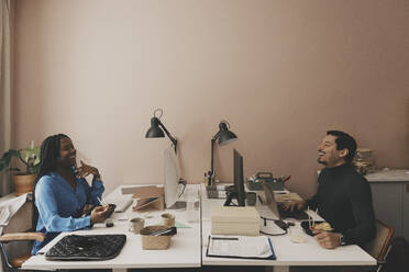 Glückliche männliche und weibliche Geschäftskollegen, die während der Mittagspause im Büro diskutieren - MASF42668