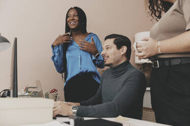 Smiling male entrepreneur sitting by female colleagues at office - MASF42674