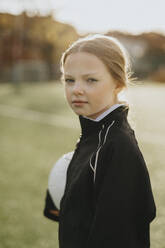 Portrait of confident elementary girl with soccer ball in sports field - MASF42696