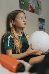 Grundschulmädchen mit Fußball, das im Schlafzimmer sitzt und nachdenkt - MASF42698