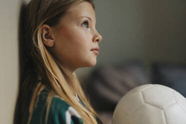 Contemplative girl with sports ball looking away at home - MASF42699