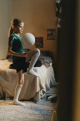 Weibliche Athletin spielt mit Fußball im Schlafzimmer zu Hause stehend - MASF42705