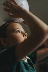 Elementary girl carrying sports ball on head at home - MASF42708