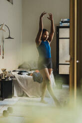 Dedicated teenage girl with hands raised exercising in bedroom at home - MASF42714