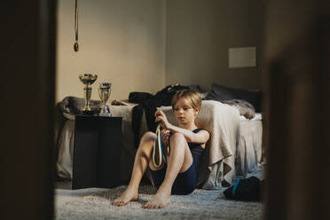 Ein Junge im Grundschulalter betrachtet eine Medaille, während er im Schlafzimmer sitzt - MASF42726