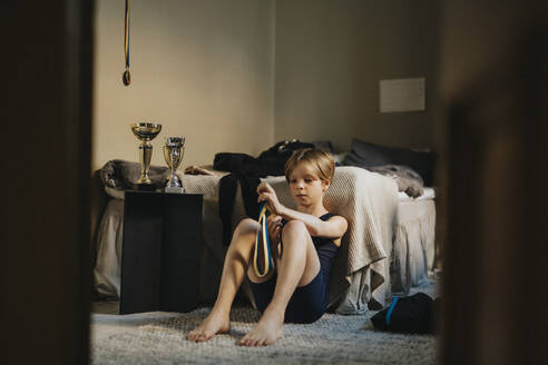 Ein Junge im Grundschulalter betrachtet eine Medaille, während er im Schlafzimmer sitzt - MASF42726
