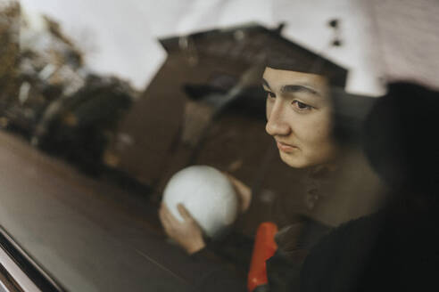 Teenage boy with soccer ball day dreaming seen through car window - MASF42737