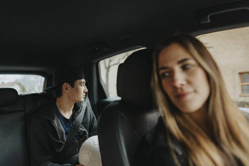 Contemplative teenage boy sitting with female coach in car - MASF42738