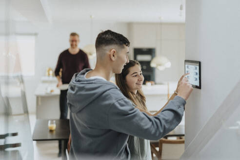 Brother and sister using digital tablet mounted on wall at smart home - MASF42801