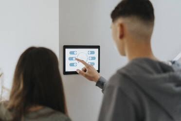 Rear view of brother and sister using digital tablet mounted on wall at home - MASF42803