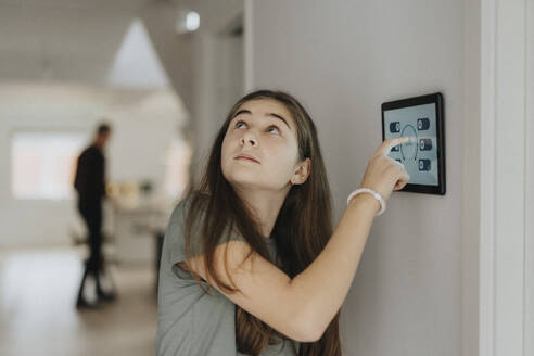 Pre-Adolescent girl adjusting room temperature through digital tablet mounted on wall at home - MASF42804