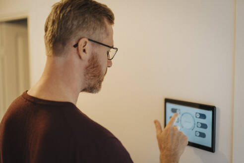 Mature man using digital tablet mounted on wall at smart home - MASF42811