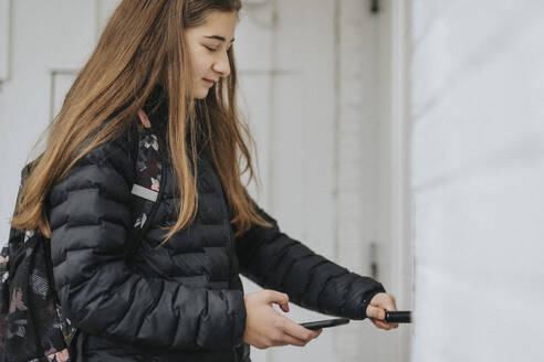 Mädchen entriegelt Türschloss mit Smartphone, während sie zu Hause steht - MASF42815