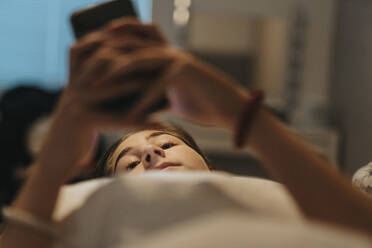 Girl text messaging on smart phone while lying in bedroom at smart home - MASF42820