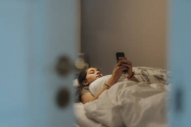 Girl using smart phone while lying on bed in bedroom at modern home - MASF42821