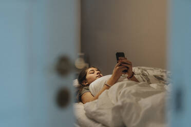 Mädchen, das ein Smartphone benutzt, während es im Schlafzimmer auf dem Bett liegt, in einem modernen Haus - MASF42821