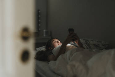 Girl using mobile phone while lying on bed in bedroom at smart home - MASF42822