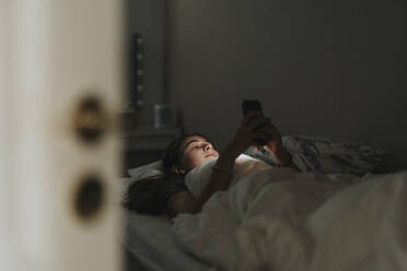 Mädchen, das ein Mobiltelefon benutzt, während es im Schlafzimmer auf dem Bett liegt, im Smart Home - MASF42822