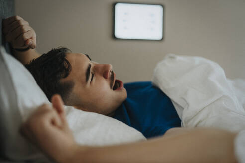 Teenage boy yawning on bed while waking up in morning at home - MASF42829