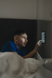 Teenage boy adjusting temperature of bedroom through digital tablet at smart home - MASF42834