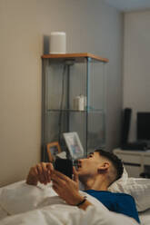 Teenage boy with smart phone lying on bed at home - MASF42836