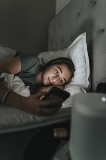 Pre-Adolescent girl using mobile phone while lying on bed in bedroom at smart home - MASF42842