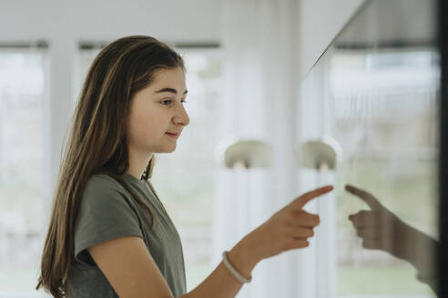 Side view of girl using smart TV while standing at home - MASF42844