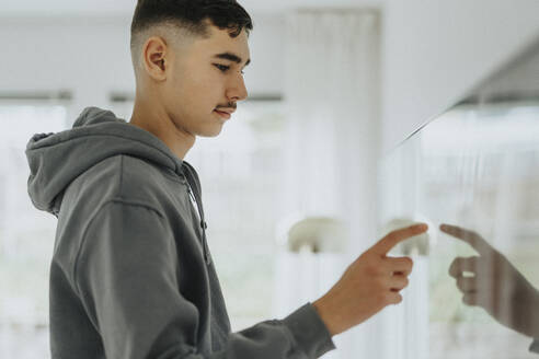 Side view of teenage boy touching smart TV screen in living room at home - MASF42846