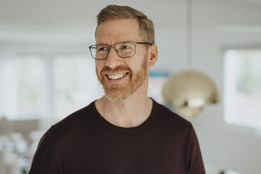 Smiling mature man wearing eyeglasses looking away at modern home - MASF42866