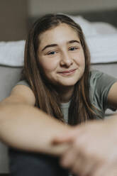 Porträt eines lächelnden vorpubertären Mädchens, das zu Hause sitzt - MASF42867