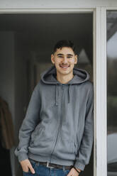 Porträt eines lächelnden Teenagers mit Hand in der Tasche, der an der Tür steht - MASF42868