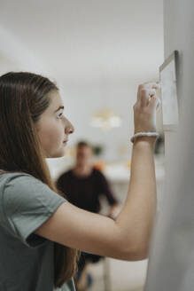 Side view of girl using home automation app through digital tablet mounted on wall - MASF42869