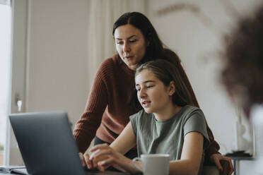 Girl using laptop sitting by mother at modern home - MASF42872