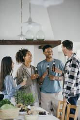 Happy friends holding alcoholic drinks while talking during dinner party at home - MASF42878