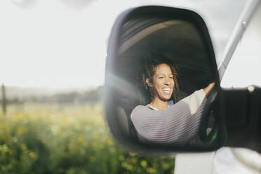 Fröhliche junge Frau am Steuer eines Lieferwagens, gesehen durch den Seitenspiegel - MASF42912