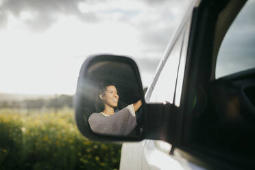 Glückliche junge Frau, die einen Lieferwagen fährt, gesehen durch den Seitenspiegel - MASF42913