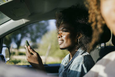 Lächelnde junge Frau, die ein Smartphone im Auto benutzt - MASF42914