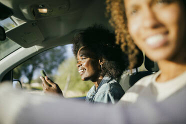 Lächelnde junge Frau mit Smartphone, die neben einem Freund im Auto sitzt - MASF42915