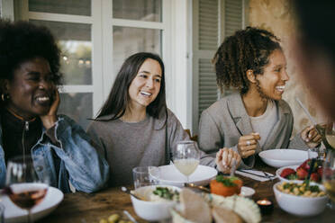 Glückliche Freundinnen sitzen zusammen am Esstisch und genießen das Abendessen im Innenhof - MASF42919