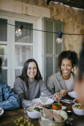 Cheerful young female friends sitting at dining table in patio for dinner party - MASF42920