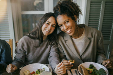 Portrait of smiling young female friends sitting at dining table in patio for dinner party - MASF42926