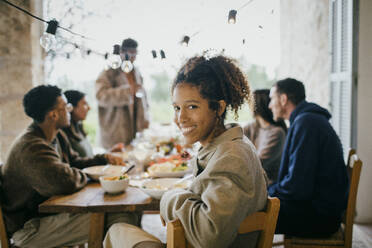 Porträt einer lächelnden jungen Frau, die mit Freunden am Esstisch sitzt, während einer Dinnerparty - MASF42935